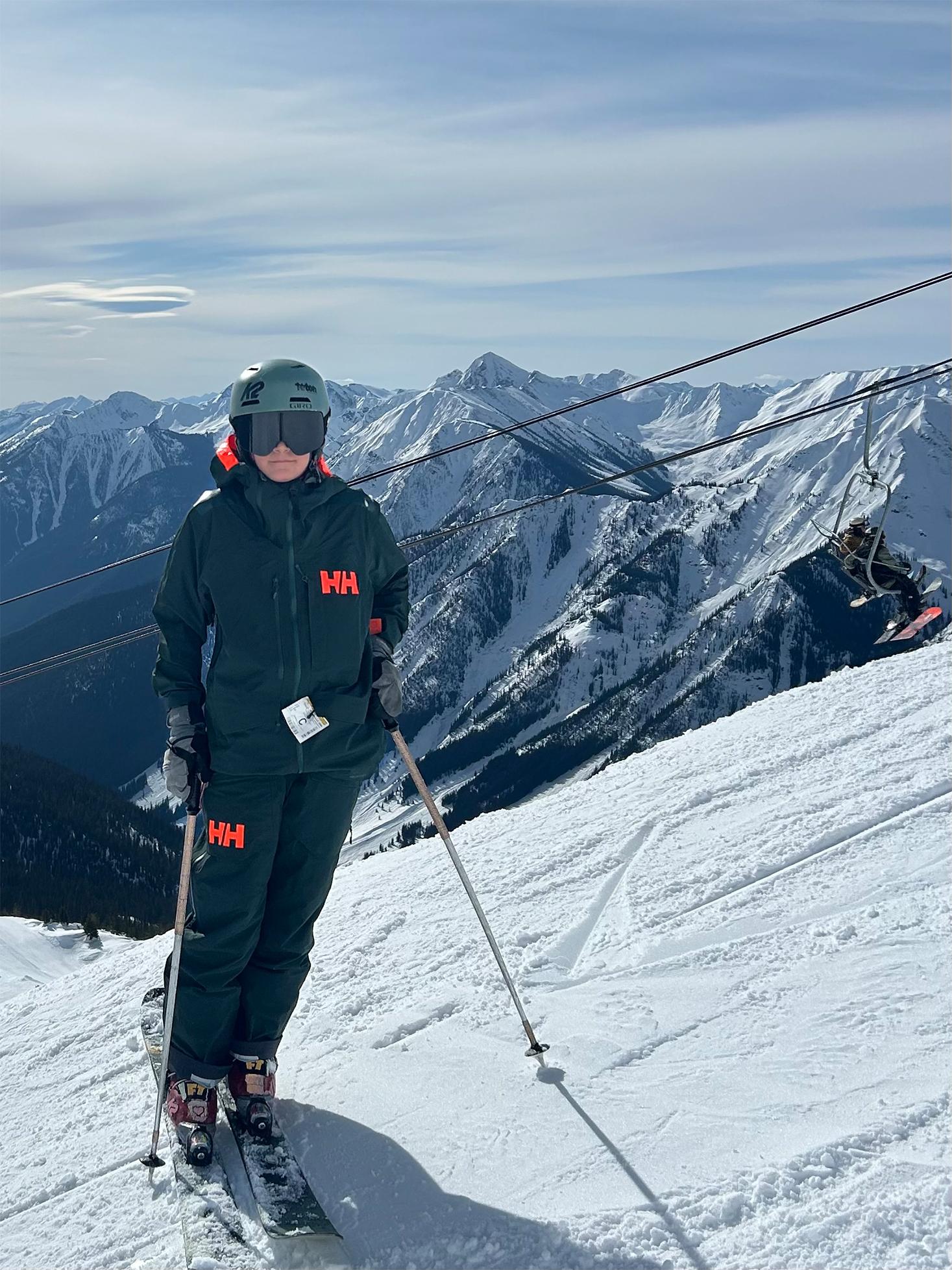 Skier on snowy mountain with distant peaks and a cloudy sky.