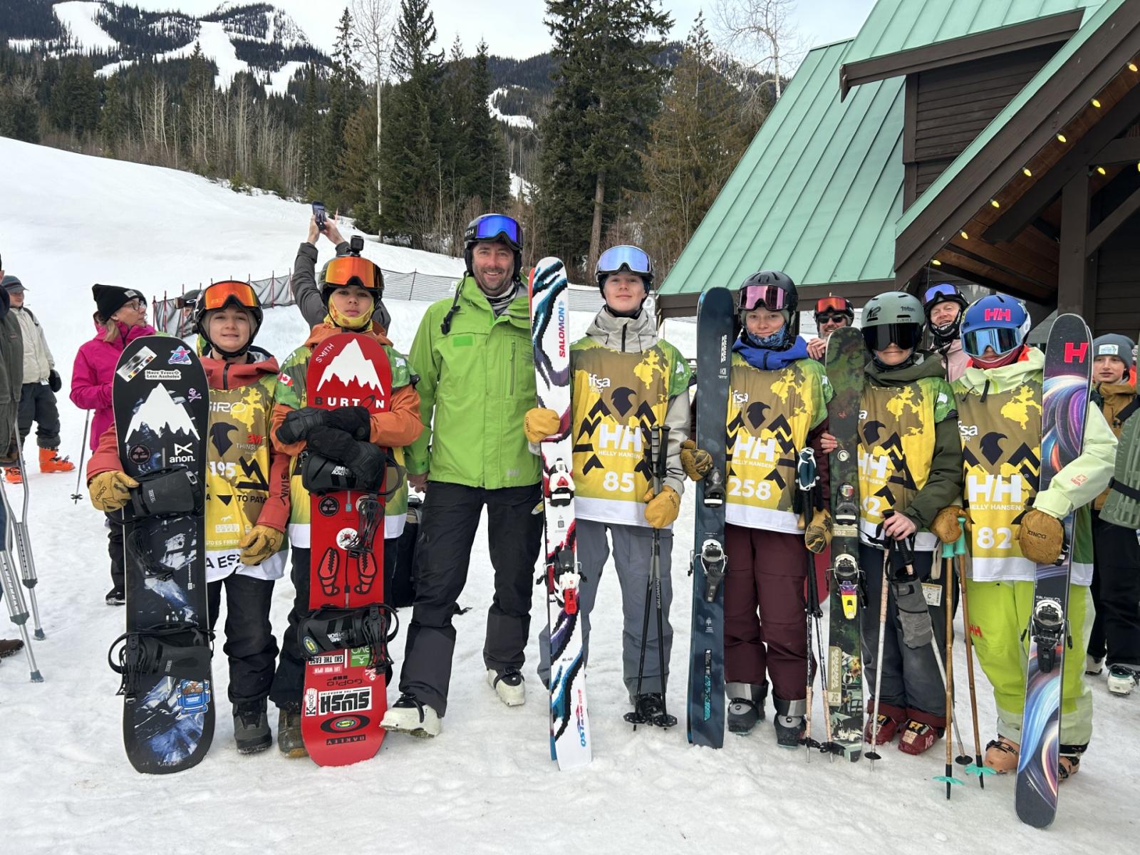 Skiers and snowboarders posing in front of a lodge on a snowy mountain.