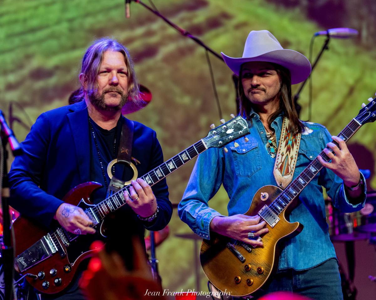Two guitarists performing on stage, one in a cowboy hat.