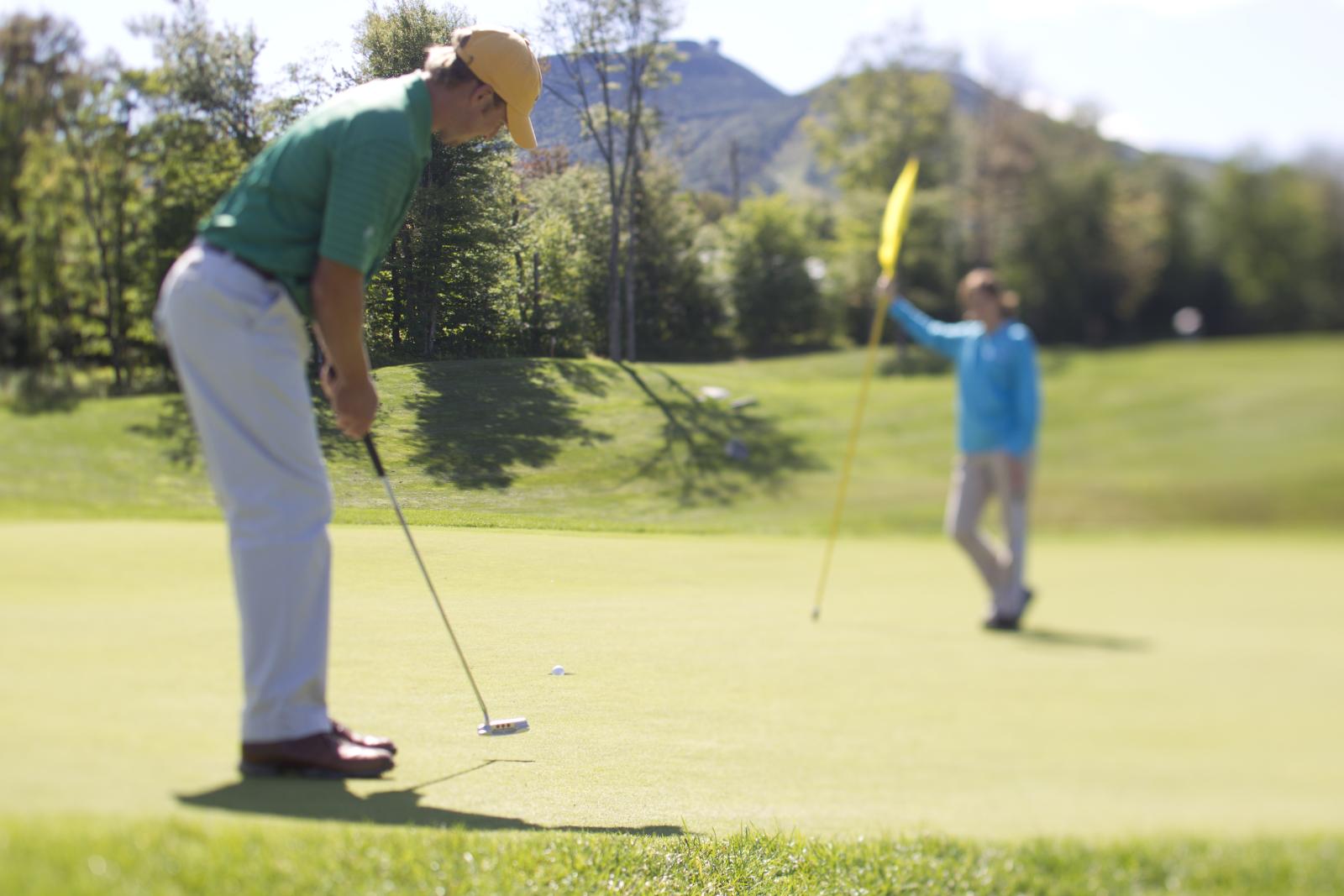 Golfer putting on a green while another person holds the flagstick.