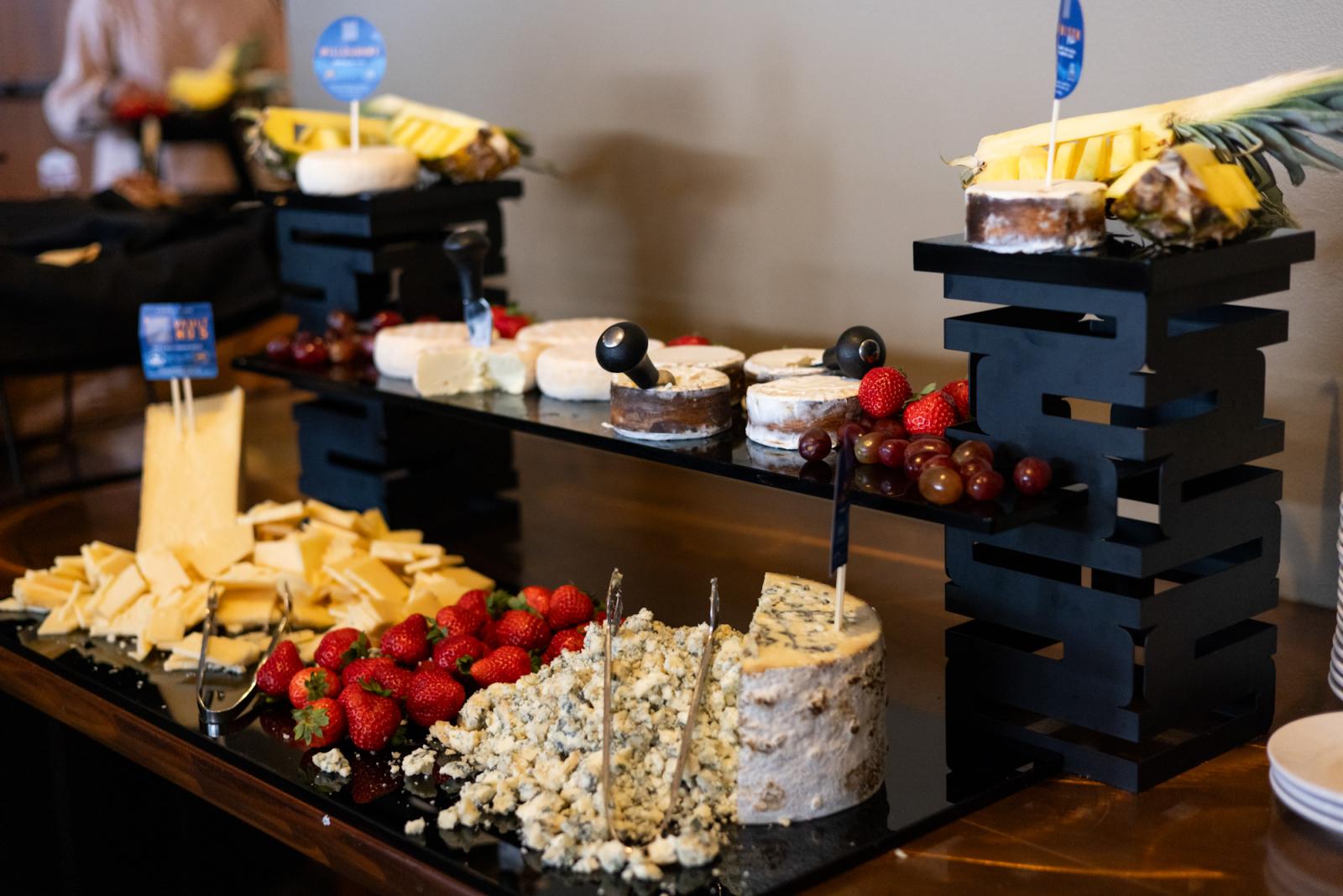 Cheese and fruit display on black stands, including grapes, strawberries, and various cheeses.