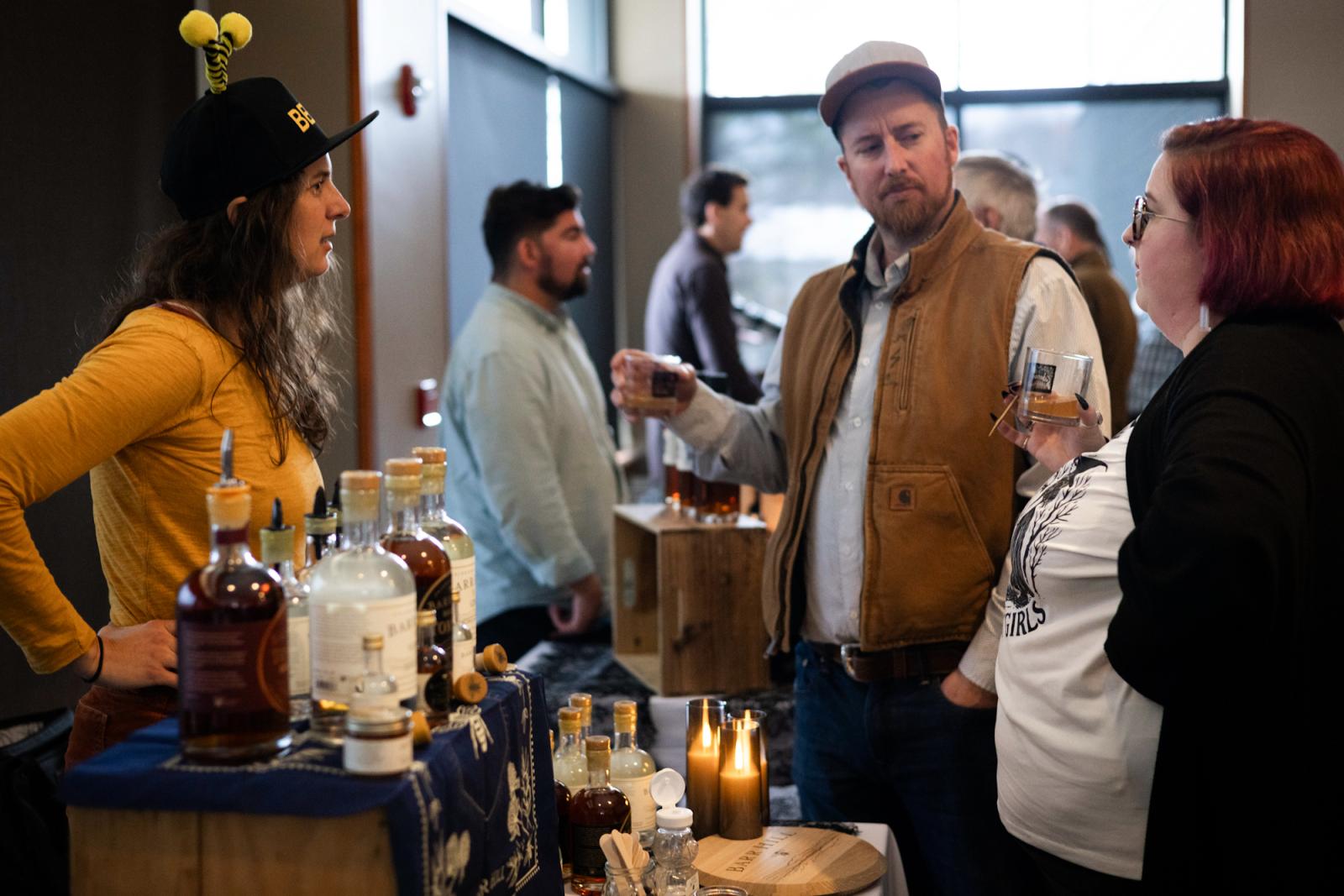 People chatting at a whiskey tasting event, surrounded by bottles.