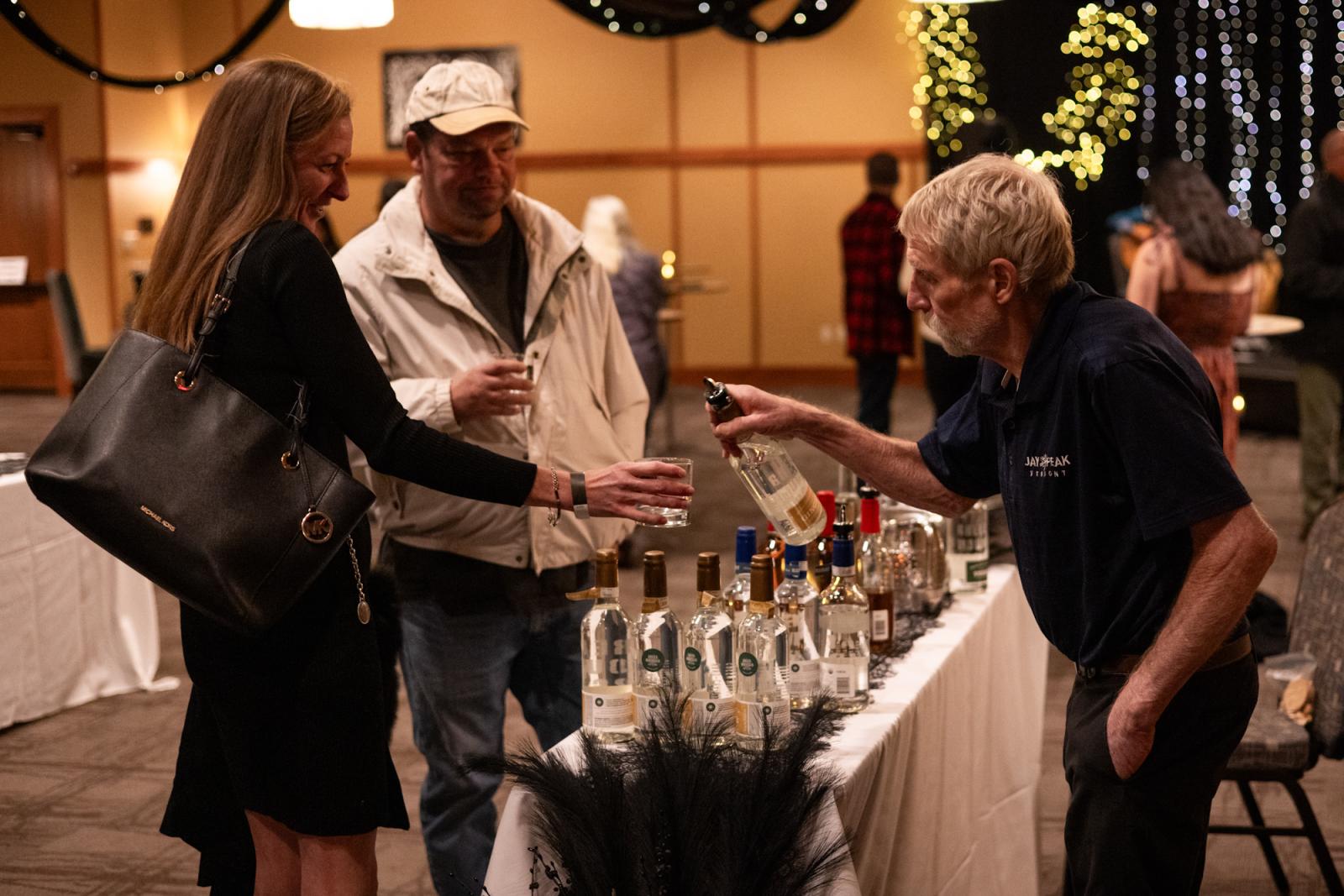 Man sampling vodka at a tasting event table with two guests.