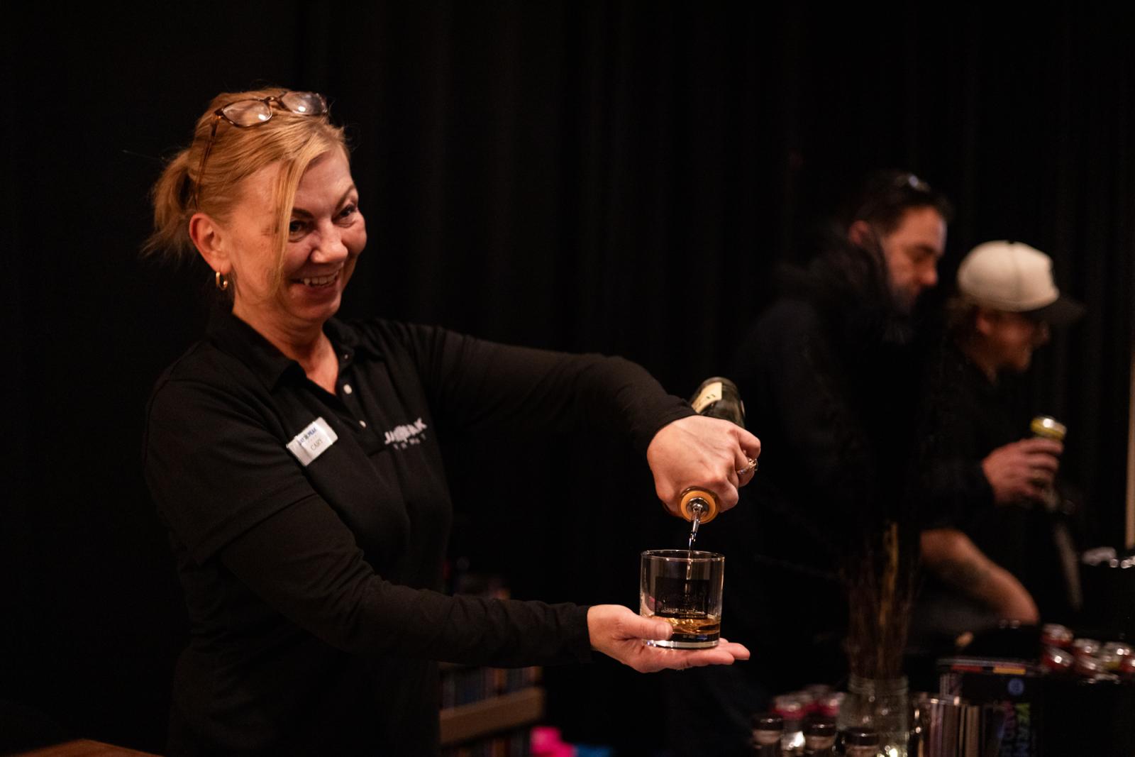 Smiling woman pours drink into a glass at an event.