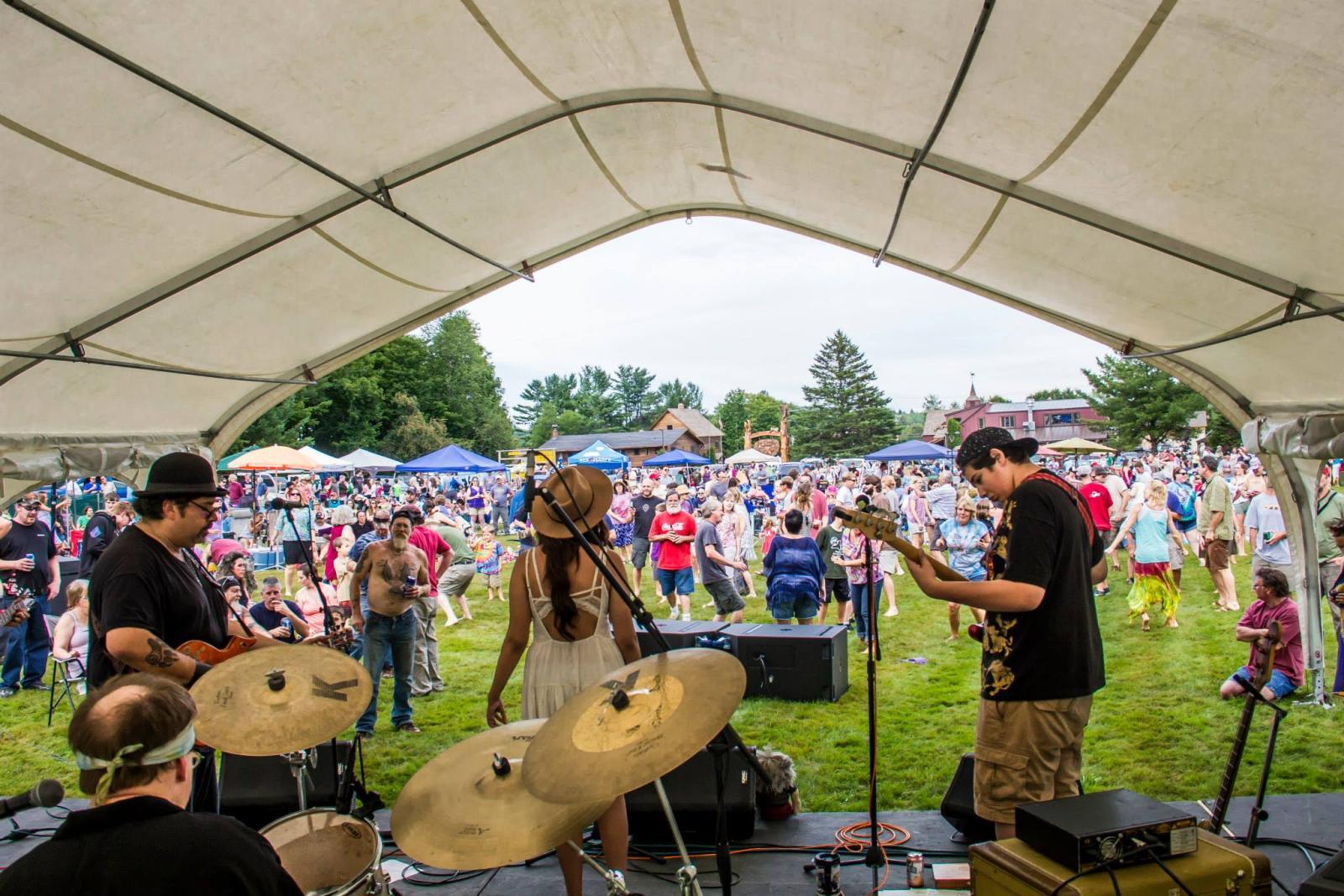 Band performing on stage at outdoor festival, large crowd watching.