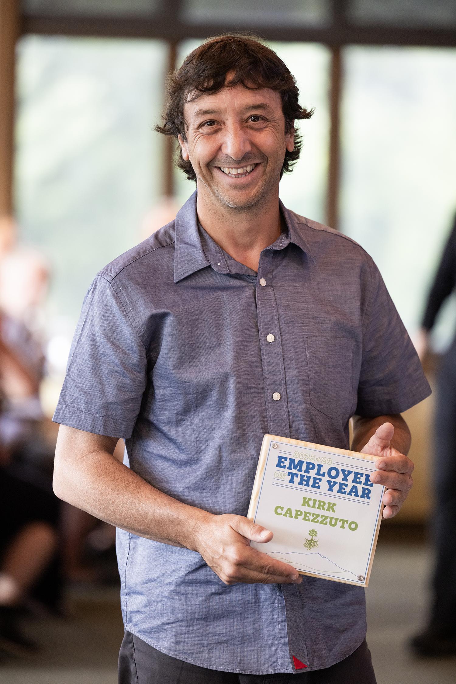 Smiling person holding Employee of the Year award indoors.