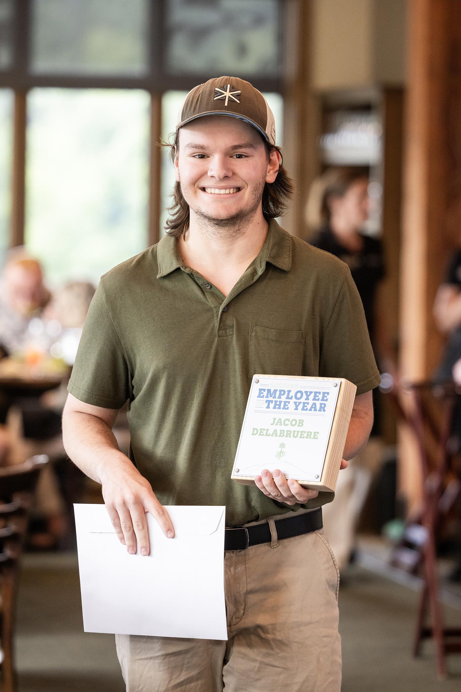 Smiling man holding an award and papers in a casual indoor setting.