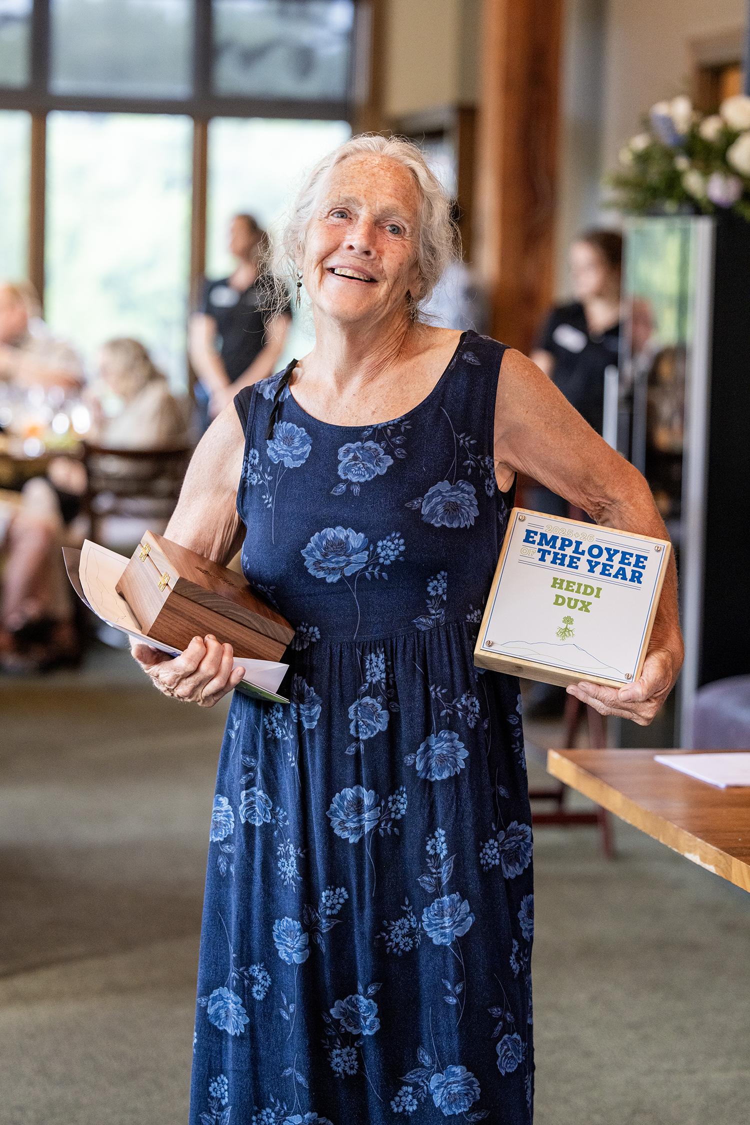 Smiling woman holding awards in a floral dress at a gathering.