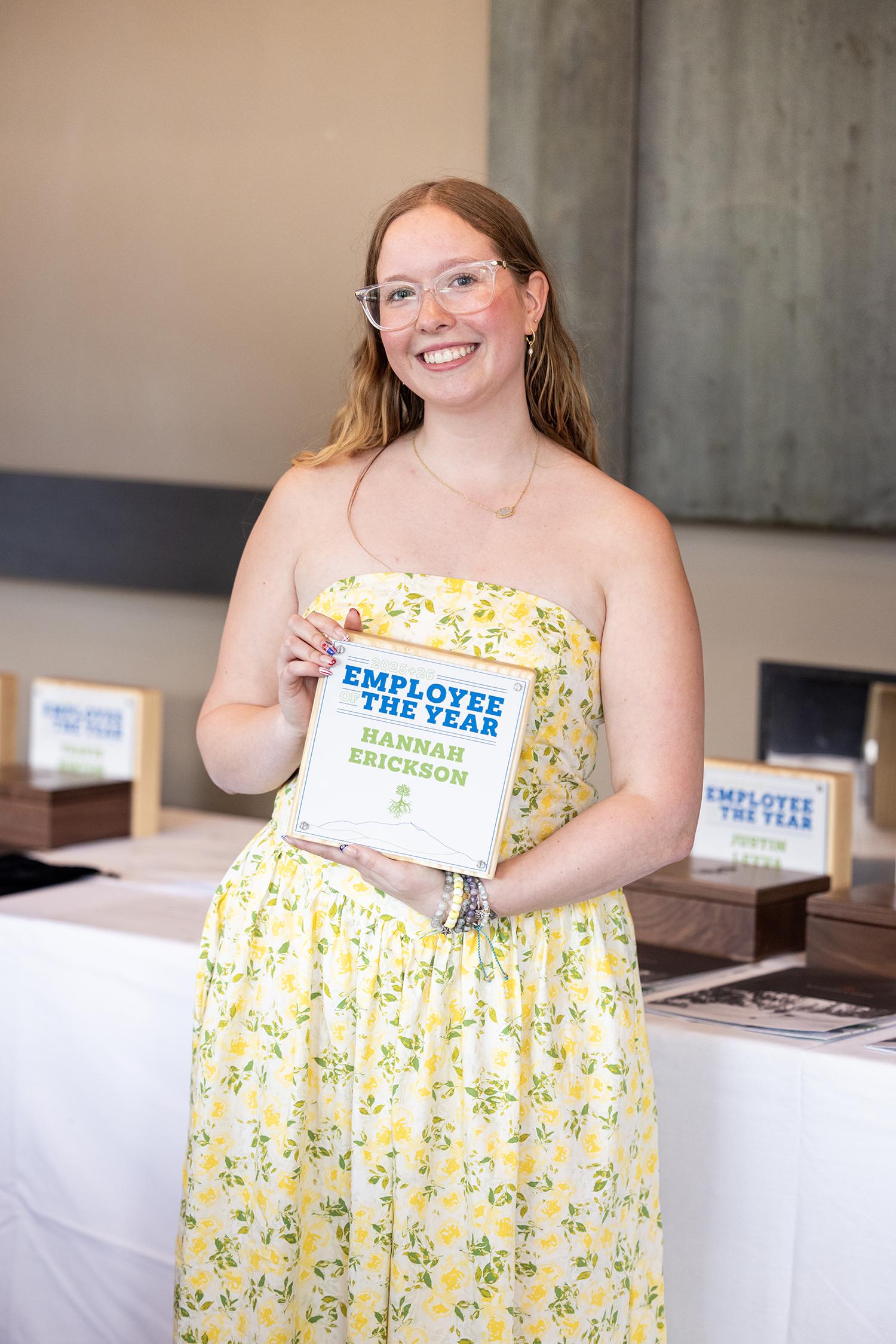 Smiling woman in a yellow floral dress holding a book.