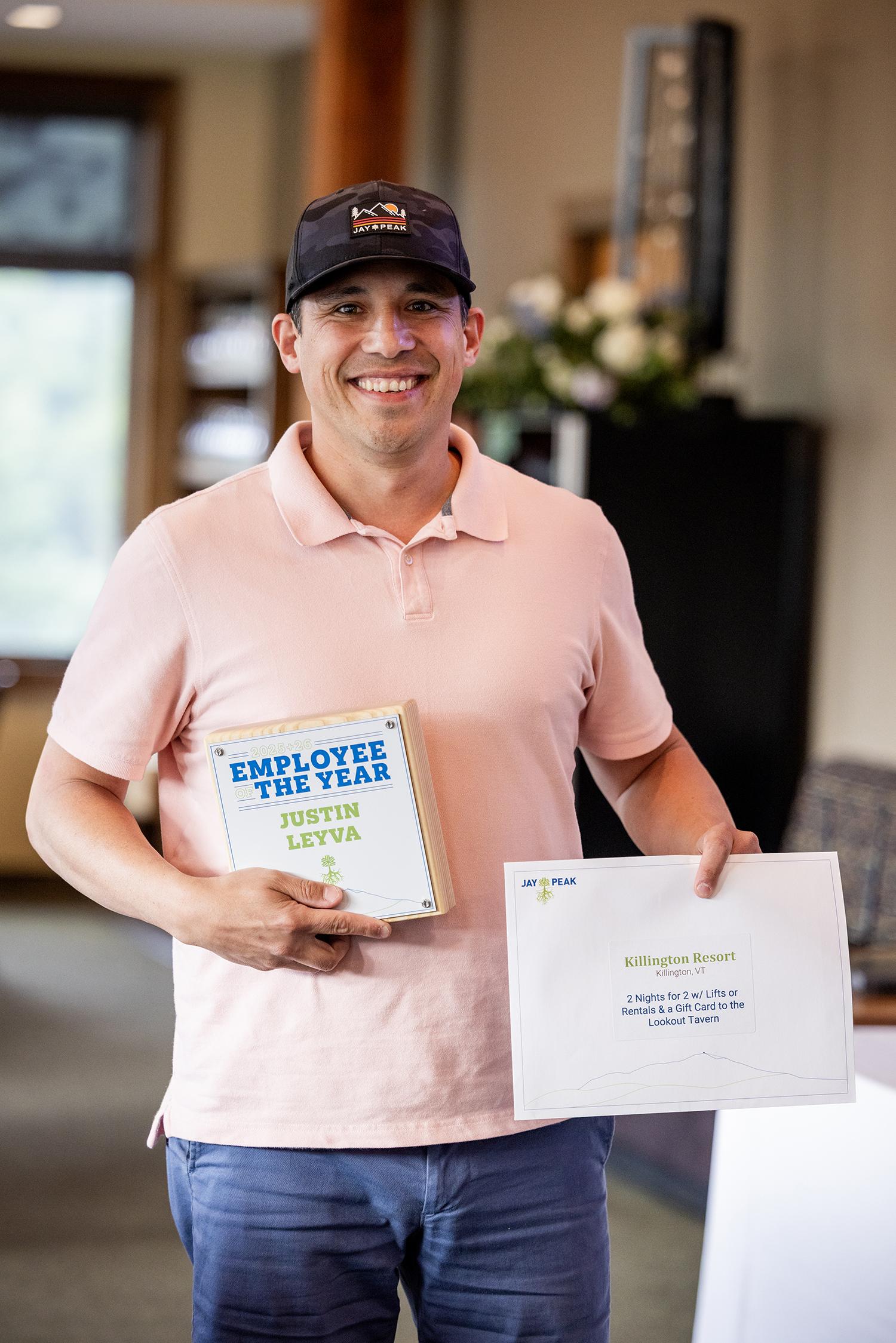 Smiling man in a pink shirt holds a book and certificate indoors.