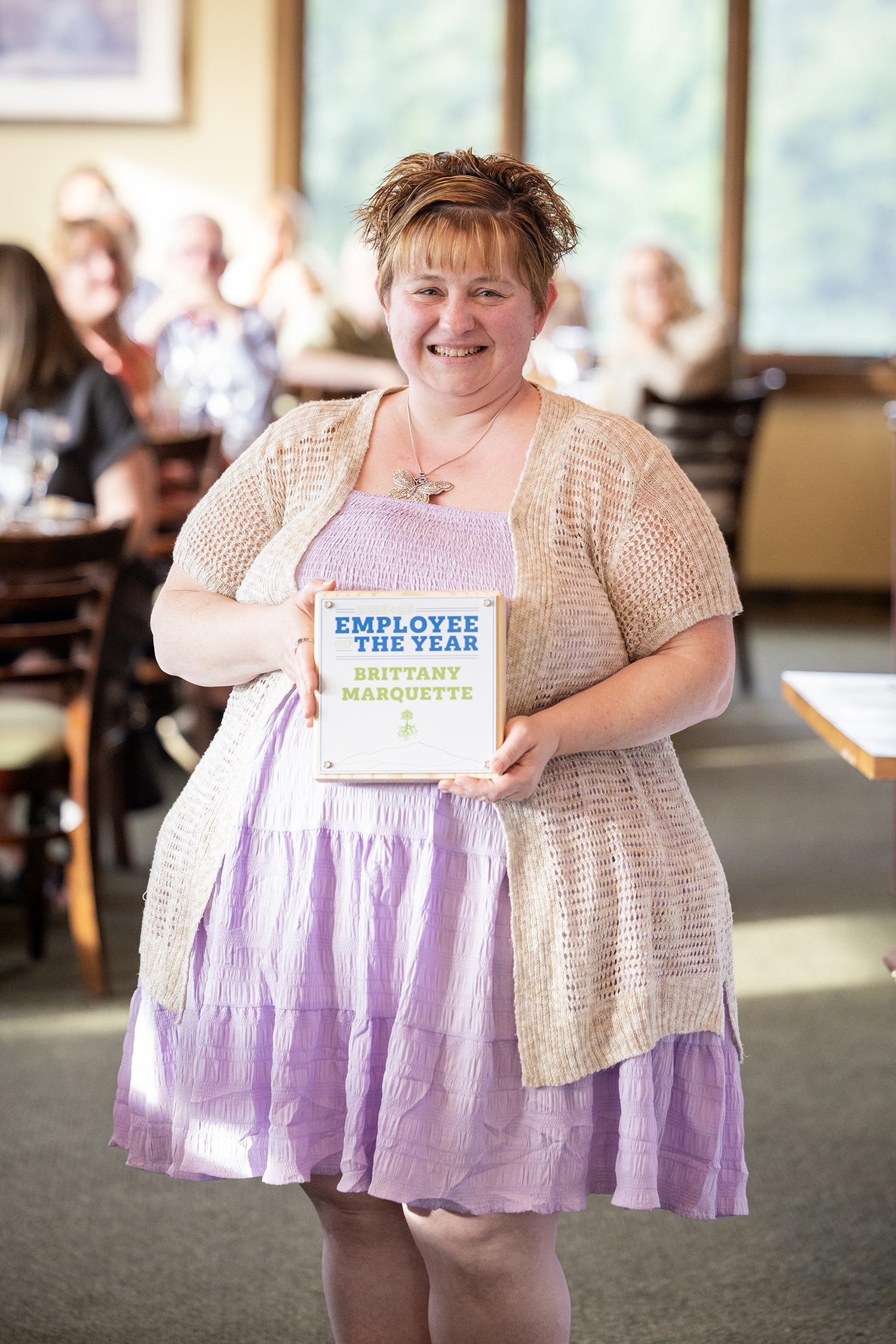 Smiling woman in a purple dress holding a book, indoors.
