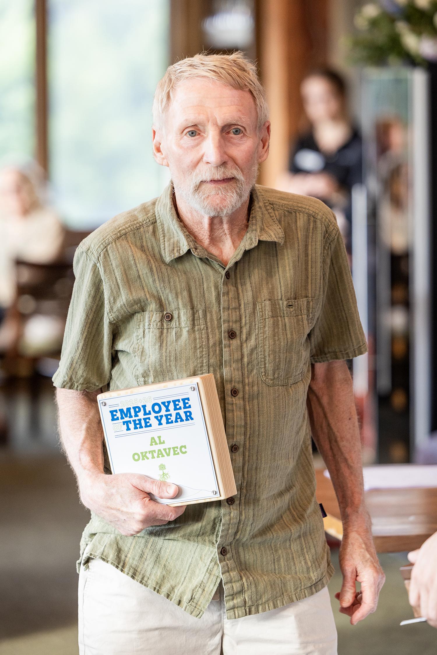 Elderly man holding a book, wearing a green shirt in a softly lit room.
