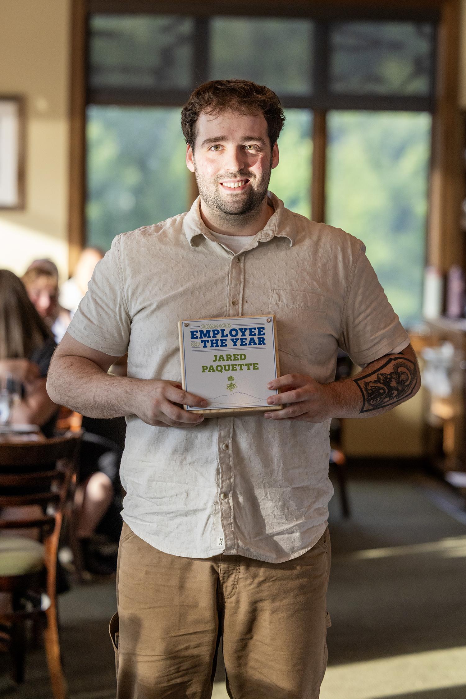 A man holding a book in a sunlit restaurant, smiling.