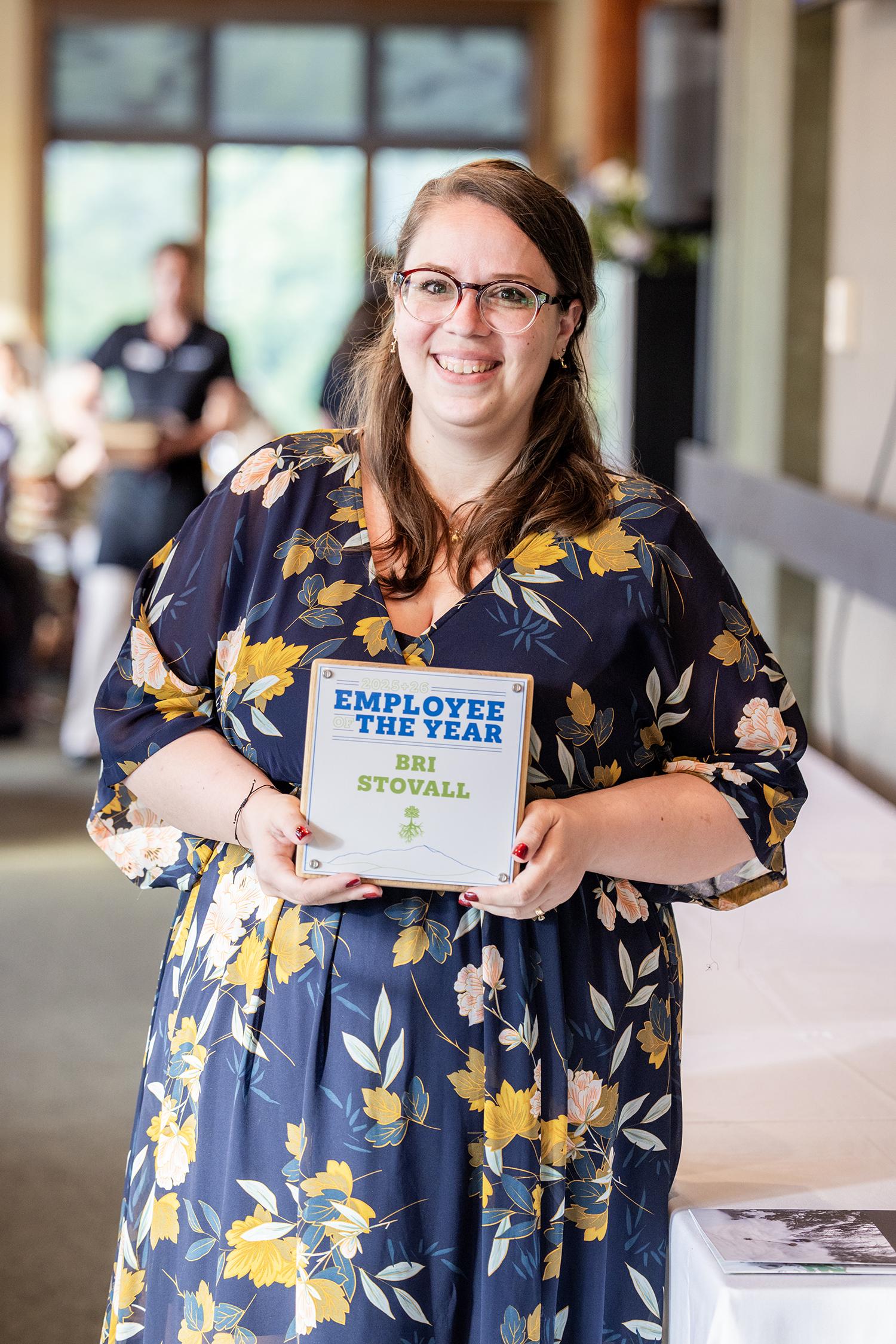Smiling woman in floral dress holding award plaque indoors.