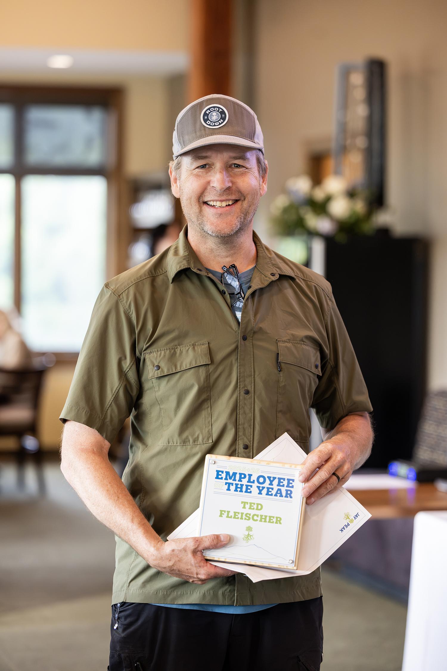 Smiling man in casual shirt and cap holding an award.