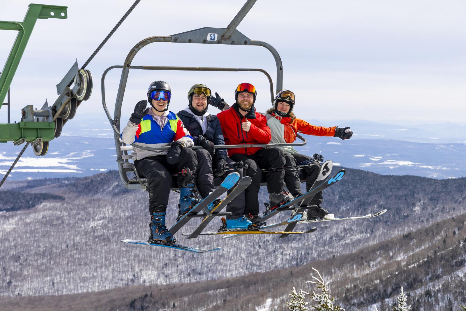 Skiers in colorful jackets on a lift, snowy mountains in the background.