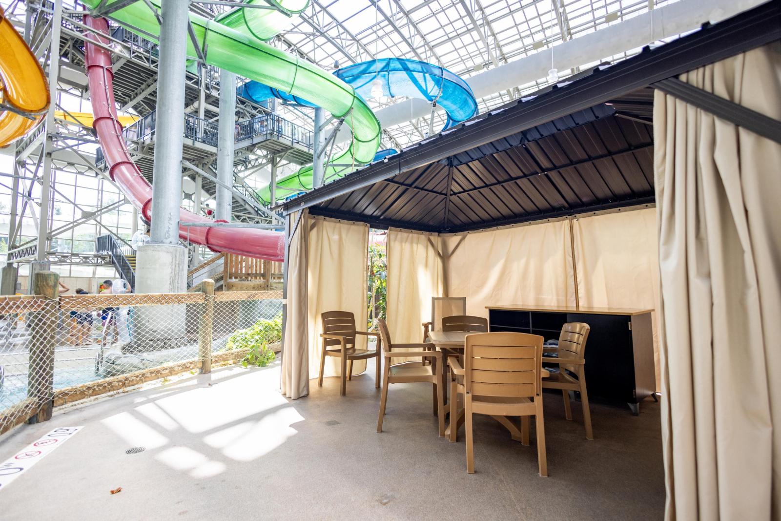 Cabana with chairs beside colorful water slides in an indoor park.