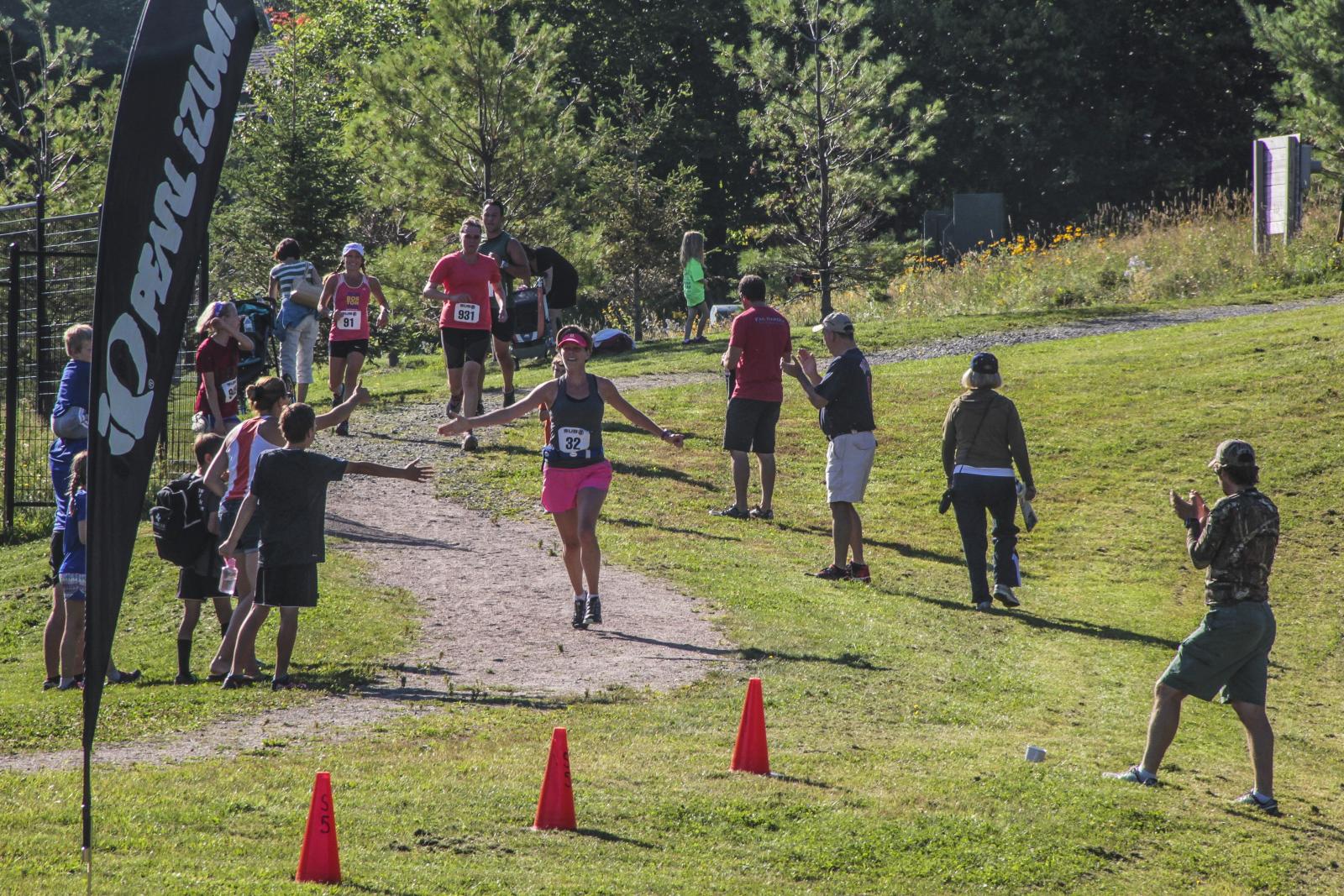 Runners and spectators gather on a grassy trail beside orange cones.