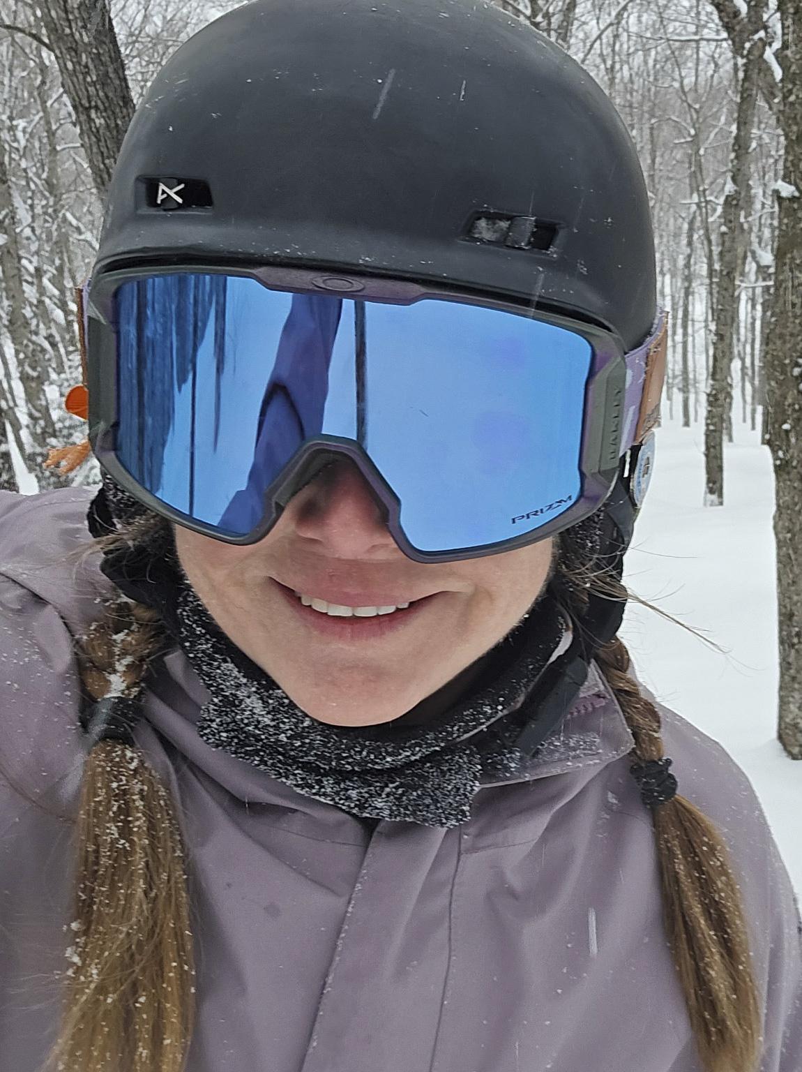 Smiling skier in helmet and blue goggles on a snowy forest trail