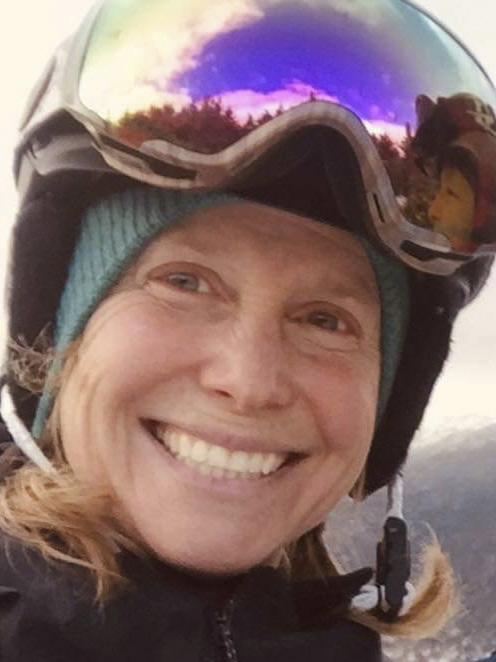 Smiling skier wearing helmet and reflective goggles on a snowy mountain.