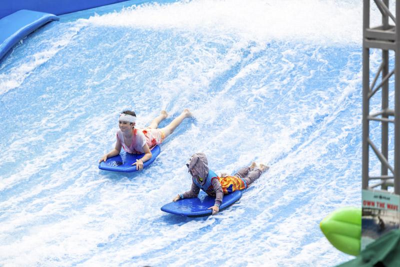 Two riders on blue inflatable tubes slide down a water park wave ramp.