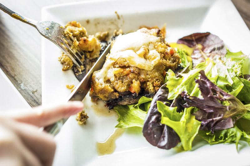 Person serving a slice of vegetable quiche with mixed green salad.
