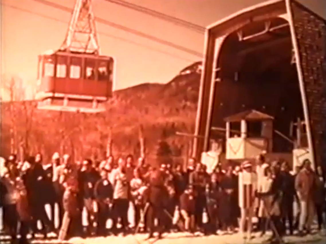 Vintage photo of a crowd gathered beneath a large cable car at a mountain station.